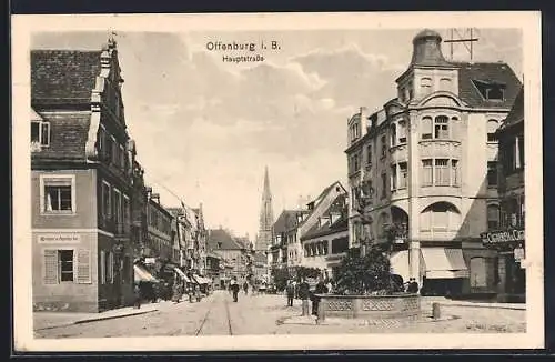 AK Offenburg i. B., Hauptstrasse mit Geschäften, Kirchturm und Burnnen