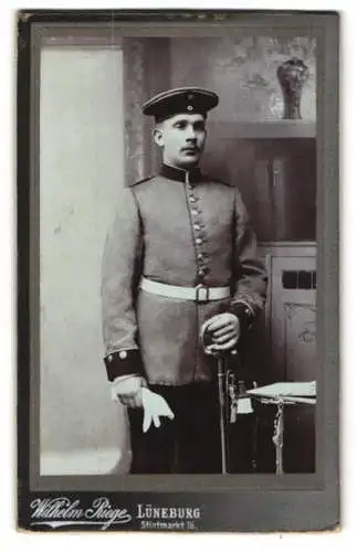 Fotografie Wilhelm Riege, Lüneburg, Soldat in Uniform mit Säbel und Portepee vor einer Studiokulisse