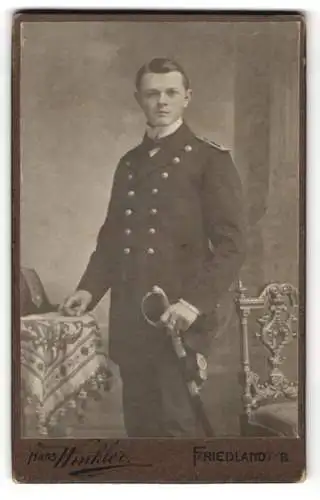 Fotografie Hans Winkler, Friedland i. B., junger Marine Offizier in Uniform mit Säben und Zweispitz auf dem Tisch