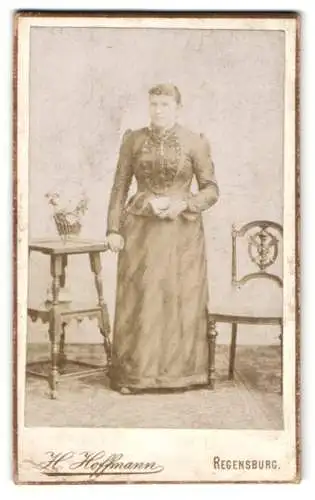 Fotografie H. Hoffmann, Regensburg, Jesuitenplatz, Frau in elegantem Kleid neben einem Tisch mit Blumen