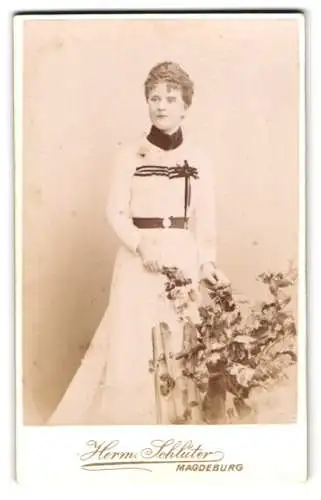 Fotografie Hermann Schlüter, Magdeburg, Breite Weg, Elegante Dame im langen Kleid neben Blumenarrangement