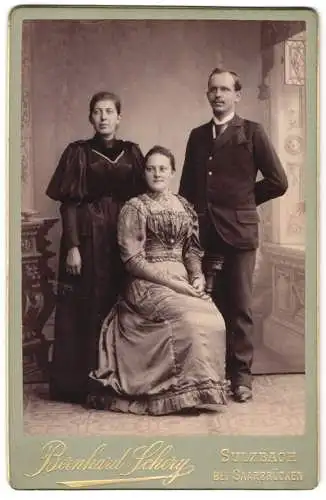 Fotografie Bernhard Schery, Sulzbach bei Saarbrücken, Stehender Mann mit zwei Frauen in eleganter Kleidung