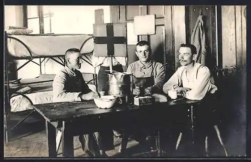 Foto-AK Drei Soldaten am Tisch vor Betten ihrer Stube, Rotkreuz-Schild