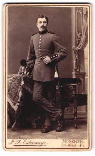 Fotografie F. H. Ostermayr, München, Soldat in Uniform nebst Raupenhelm auf dem Tisch