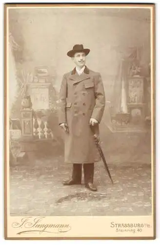 Fotografie J. Jungmann, Strassburg i. E., junger Mann im Trenchcoat mit Schirm und Hut