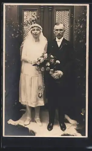 Foto-AK Braut im weissen Kleid mit Bouquet neben ihrem Bräutigam im Anzug auf einem Pelz, Hochzeit