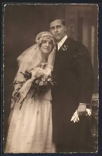 Foto-AK Braut im weissen Kleid mit Bouquet neben ihrem Bräutigam mit grossen Augen im Anzug, Hochzeit