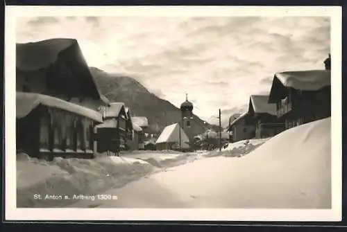 AK St. Anton am Arlberg, Strassenpartie mit Kirche im Winter