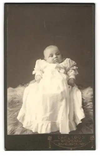 Fotografie Carl Loos, Weidenau, Wilhelmstr. 79 /2, Baby in weissem Kleid auf Fell