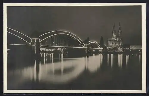 AK Köln a. Rh., Kölner Dom und Brücke bei nächtlicher Beleuchtung