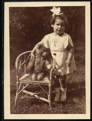 Fotografie unbekannter Fotograf und Ort, niedliches kleines Mädchen mit ihrem Teddybär auf dem Stuhl