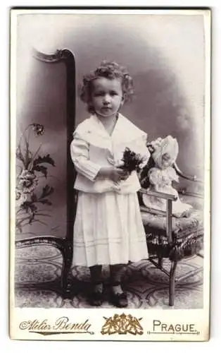 Fotografie Benda, Prague, Mädchen Helene Fischbach im weissen Kleid mit Puppe auf Stuhl