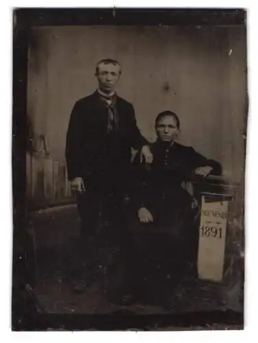 Fotografie Ferrotypie Mann und Frau in dunkler Kleidung vor einer Stdiokulisse, Souvenier 1891