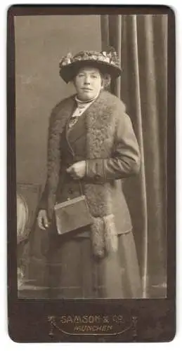 Fotografie Samson & Co., München, Dame im dunklen Kleid mit Pelzstola und Handtasche, geschmückter Hut