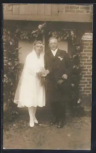 Foto-AK Lächelndes Brautpaar vor geschmückter Haustür