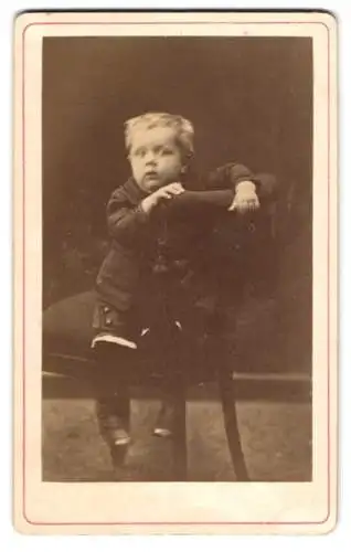 Fotografie unbekannter Fotograf und Ort, kleiner Knabe posiert verkehrt herum auf einem Stuhl