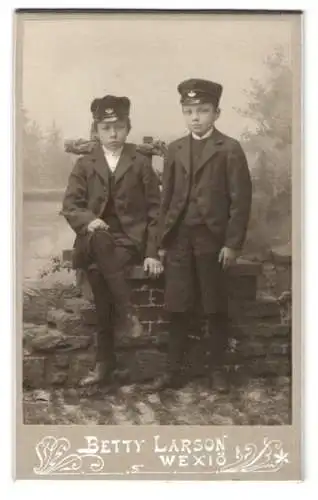 Fotografie Betty Larson, Wexiö, Zwei Jungen in Anzügen und Schirmmützen