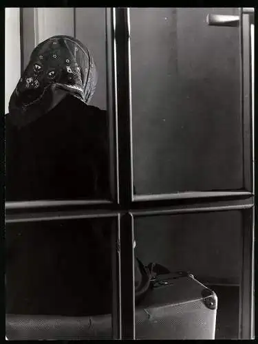 Fotografie Eckelt, Berlin, ältere Dame mit Kopftuch sitzt auf ihren Koffer zur Abreise, Schnappschuss
