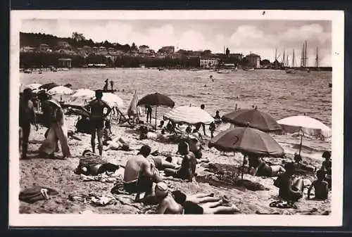 AK Sainte-Maxime, La plage animée avec parasols et voiliers en arrière-plan