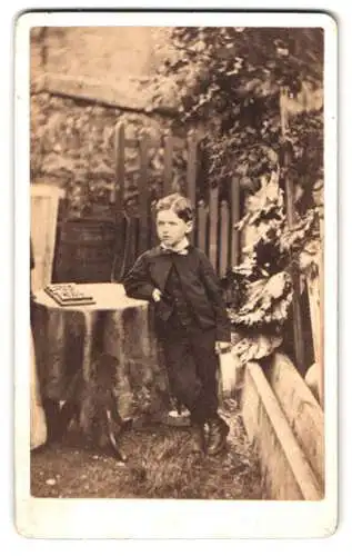 Fotografie unbekannter Fotograf und Ort, Junge im Garten neben Tisch