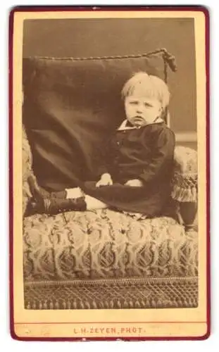 Fotografie L.H. Zeyen, Liège, Place S. Jean 1, Porträt eines Kleinkindes auf einem Polsterstuhl