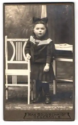 Fotografie Max Goldschmidt, Oederan i. S., Kind in Matrosenanzug vor Stuhl im Atelier