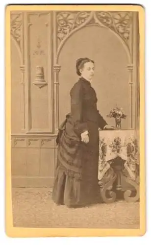 Fotografie Josef Poestion, Aussee, Frau stehend neben Tisch mit Blumenvase