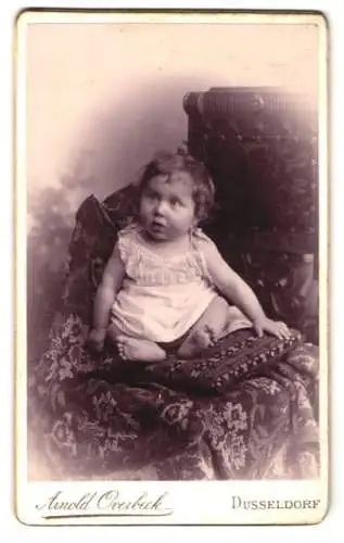 Fotografie Arnold Overbeck, Düsseldorf, Königsallee 43, Kleinkind auf dekorativem Stuhl sitzend