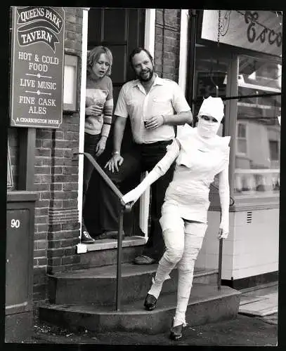 Fotografie junge Frau in Stapsen als Mumie verkleidet verlässt einen Pub, Grossformat 20 x 25cm