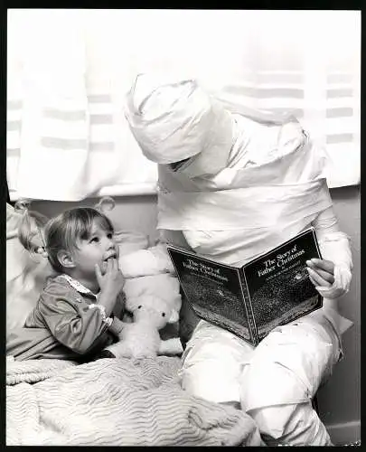 Fotografie Mutter verkleidrt als Mumie liest ihrer Tocher aus The Story of Father Christmas vor, Grossformat 21 x 25cm