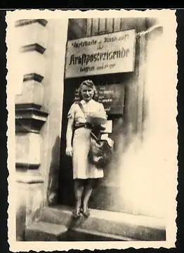 Fotografie jung Briefträgerin / Postbotin mit Posttasche vor der Wartehalle für Kraftpostreisende