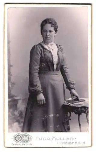 Fotografie Hugo Müller, Freiberg i. S., Fischerstrasse 29, Frau in elegantem Kleid stehend neben Tisch