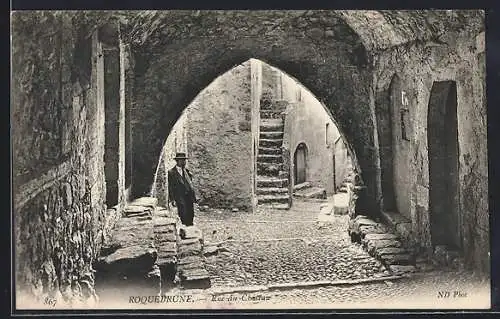 AK Roquebrune, Rue du Château sous une arche en pierre avec un homme élégant