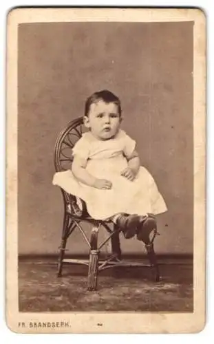 Fotografie Fr. Brandseph, Stuttgart, niedlicher kleiner Junge Mark im Kleidchen auf einemm Stuhl sitzend