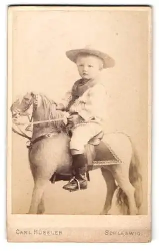 Fotografie Carl Hüsseler, Schleswig, junger Knabe im Sommeranzug auf grossen Spielzeugpferd sitzend