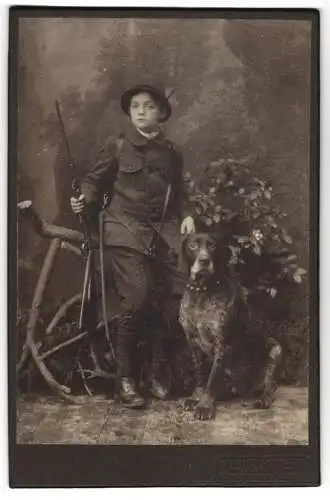 Fotografie Atelier Schmidt, Tharandt, junger Knabe Hellmuth Kleber als Jäger mit Gewehr und Jagdhund samt Peitsche
