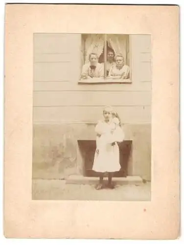 Fotografie unbekannter Fotograf und Ort, kleines Mädchen mit Puppe vor dem Wohnhaus, Familie schaut aus dem Fenster