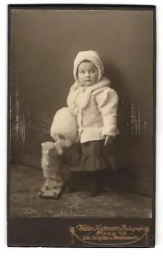 Fotografie Walter Taubmann, Pirna a. E., kleines Mädchen Ilse im Wintermantel mit Muff und Stoffschaf auf Rollen