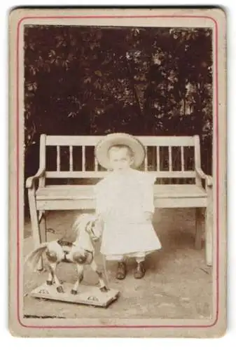Fotografie unbekannter Fotograf und Ort, kleines Kind im Kleid mit Holzpferd auf Rollen