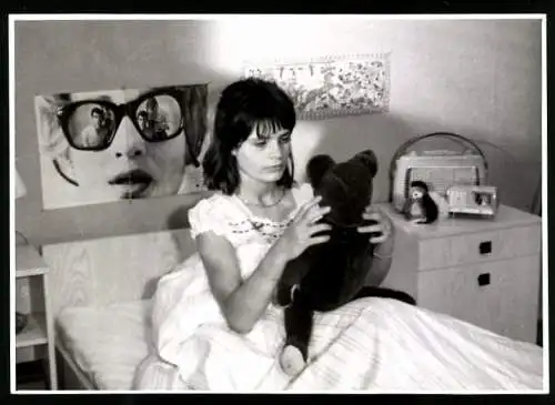 Fotografie Nordmark-Film, Kiel, junge Frau mit Teddybär im Bett, Filmteam spiegelt sich in der Brille auf Portrait