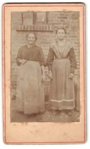 Fotografie unbekannter Fotograf und Ort, Zwei Frauen vor Backsteinmauer