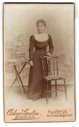 Fotografie Oskar Goetze, Berlin, Paul Str. 26, Frau in elegantem Kleid neben Stuhl
