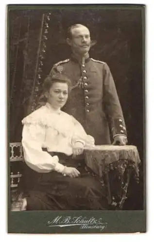 Fotografie M. B. Schultz, Flensburg, Paarporträt, Dame und Uffz. in Uniform mit Schützenschnur 2. Stufe