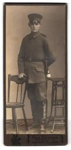 Fotografie Paul Bänder, Muskau, Schmalzstr. 129, Soldat in feldgrauer Uniform mit Bajonett und Schirmmütze