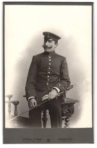 Fotografie Atelier Thiele, Hanau a.M., Westbahnhof, Einjährig-Freiwilliger in Uniform mit Säbel und Schirmmütze, 1902