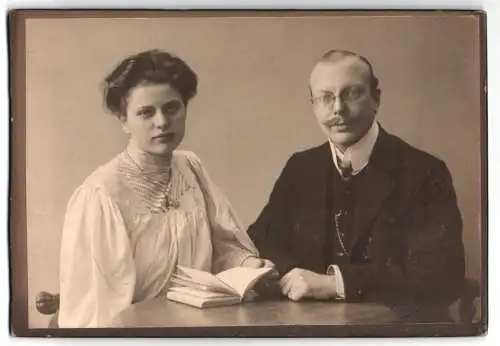 Fotografie unbekannter Fotograf und Ort, Elegantes Paar an Tisch mit Buch