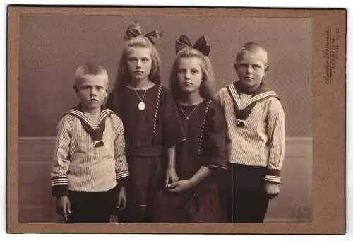 Fotografie Atelier Remmer, Langballig, Vier Kinder in Matrosenanzügen und in dunklen Kleidern mit Haarschleife