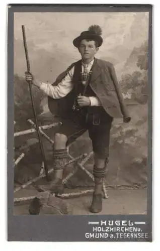 Fotografie Hugel, Holzkirchen, Gmund a. Tegernsee, junger Mann in traditioneller Tracht mit Lederhose und Wanderstab
