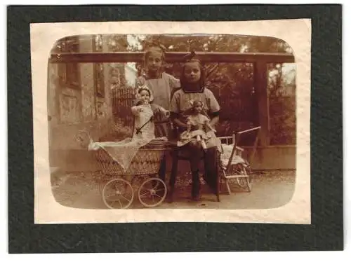 Fotografie unbekannter Fotograf und Ort, Zwei Mädchen mit Puppen und Puppenwange im Garten