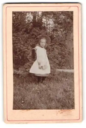 Fotografie unbekannter Fotograf und Ort, kleines Mädchen im Garten mit Schulranzen, Einschulung